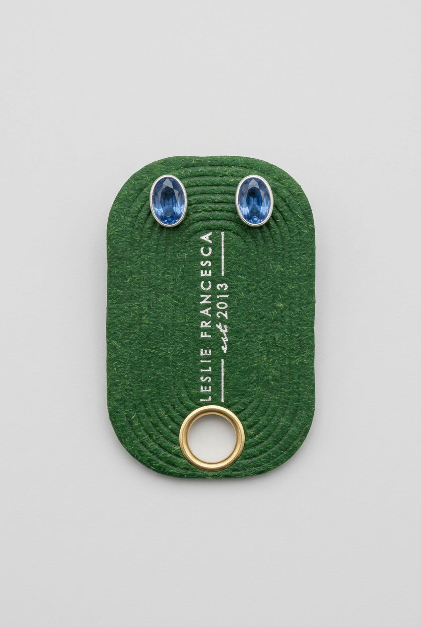  Two oval blue gemstones  'LESLIE FRANCESCA' and 'EST.2015', placed on a light wood grain surface.