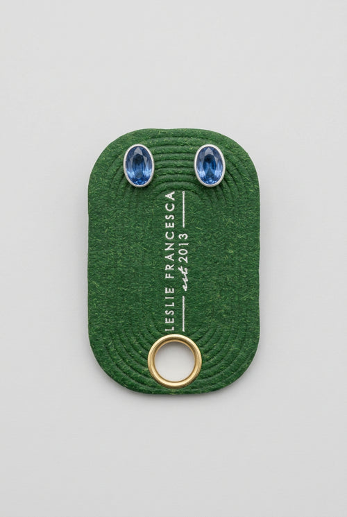  Two oval blue gemstones  'LESLIE FRANCESCA' and 'EST.2015', placed on a light wood grain surface.